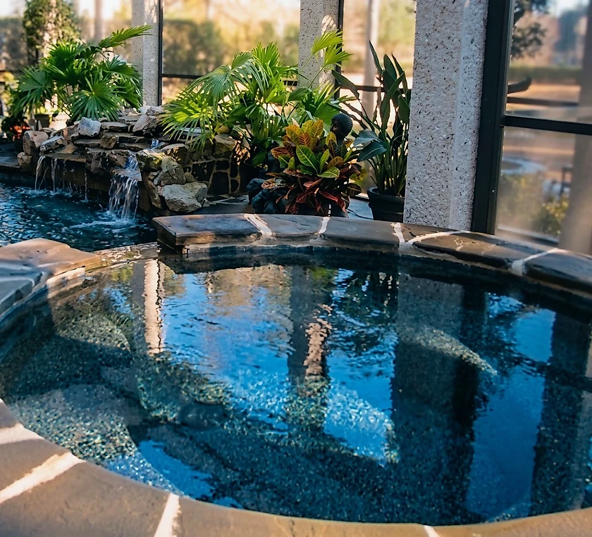 A dark, planted indoor pool and spa with a rock waterfall